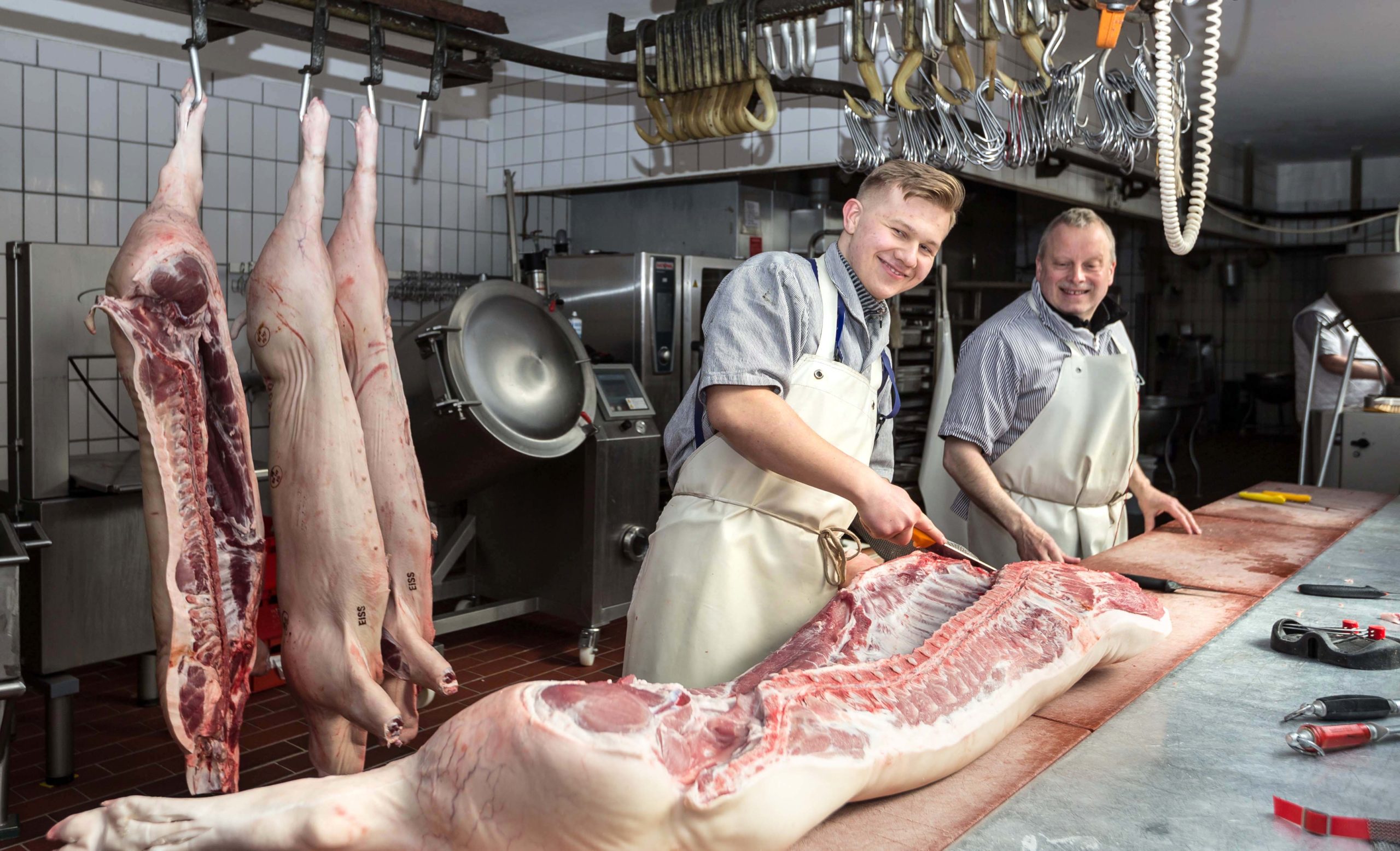 Philipp Klekla freut sich über Tipps von Fleischermeister Ulrich Rotzoll, denn beim Zerlegen von Schweinehälften gibt es für den Auszubildenden einiges zu lernen. 