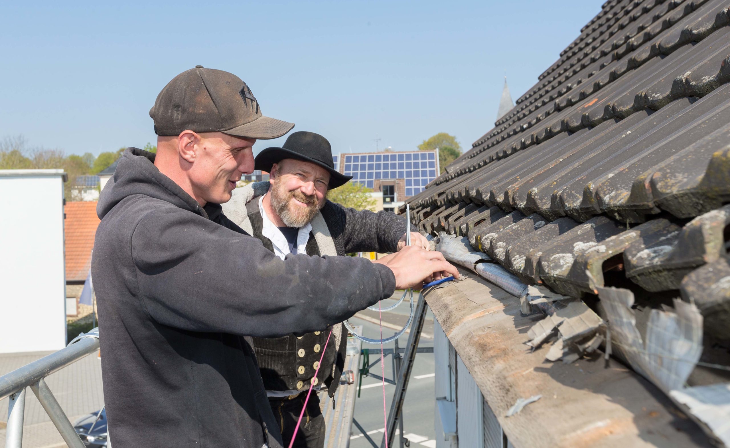 Geselle Yves Viert und Dachdeckermeister Thomas Gutwin richten gemeinsam Rinneisen aus, in die später die Dachrinne eingehängt wird.     
