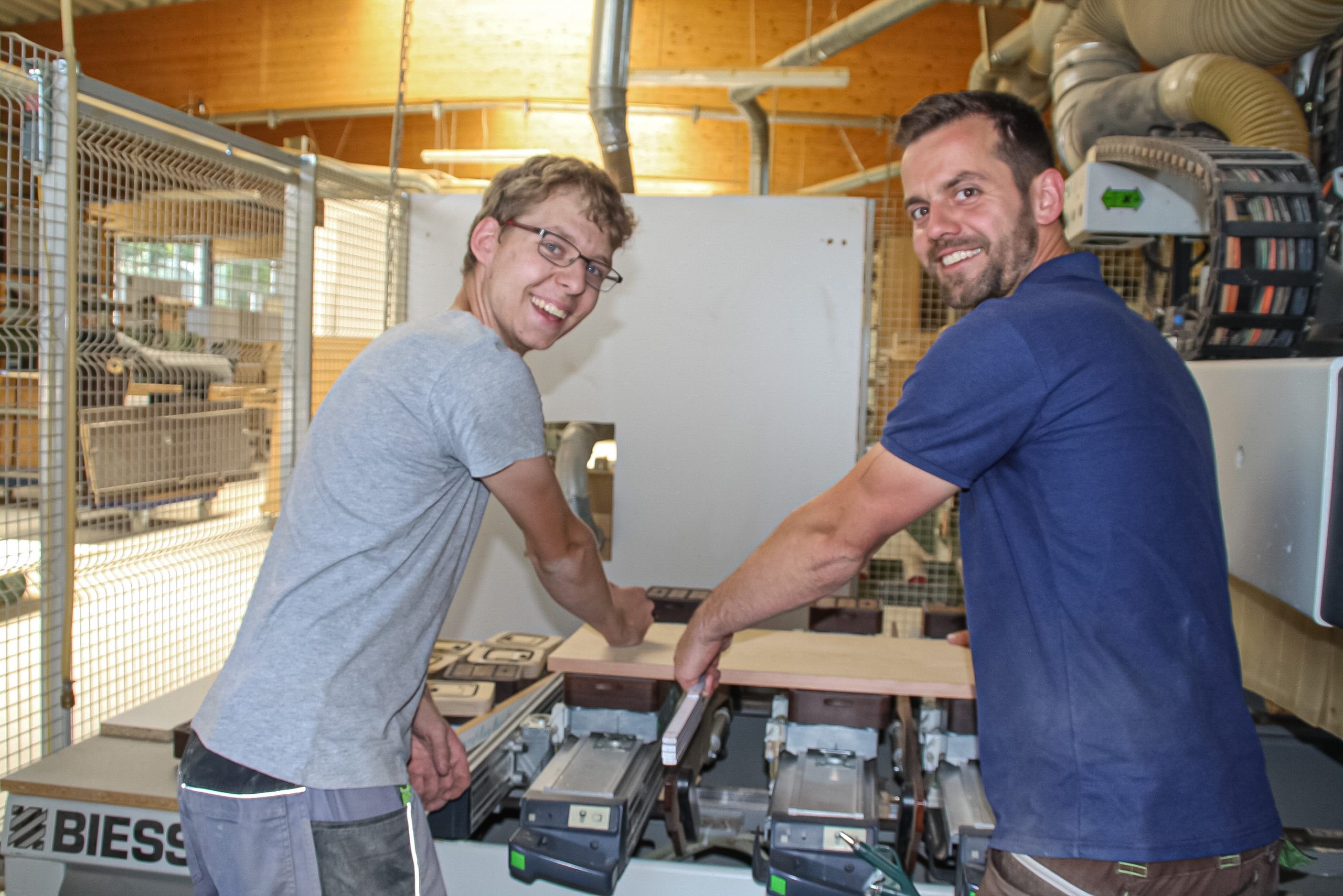 Auszubildender Manuel Koppius und Tischlermeister Julian Schiermeister bereiten gemeinsam an der CNC-Maschine Fräs- und Bohrarbeiten für die Korpusseiten eines individuell gefertigten Schrankes vor. 
